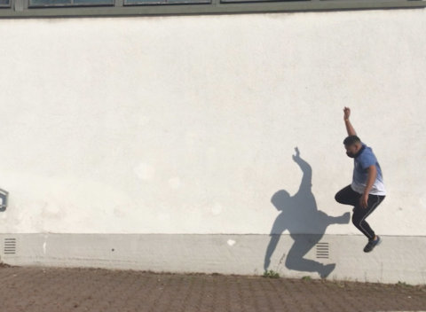 Filmauschnitt: ein Schüler springt, tanzt im Hof, Schattenriss an der Wand